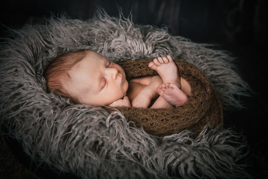 Baby liegt am Rücken auf einm Fell und schläft