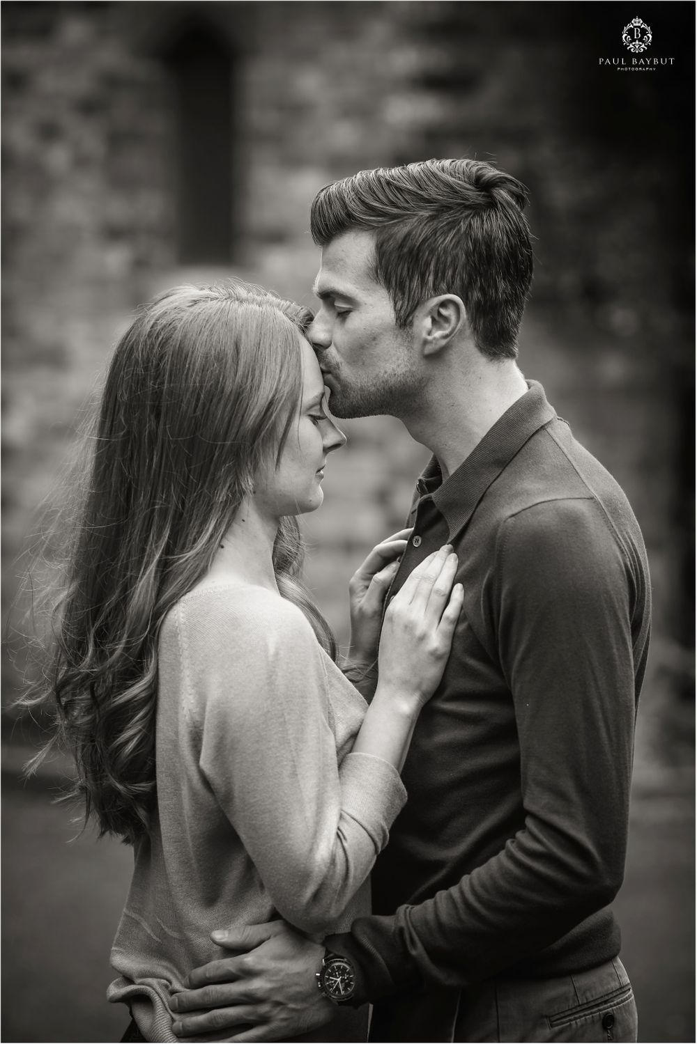 Male kisses female tenderly on the forehead whilst they hold each other in the park