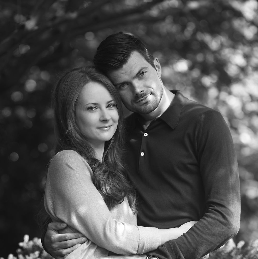 Newly engaged Manchester couple hug each other under the leaves of a tree in a Manchester park