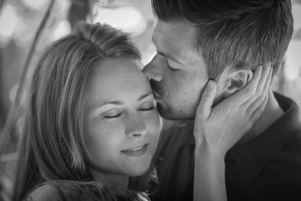 Female holds her fiancé as he kisses the side of her face