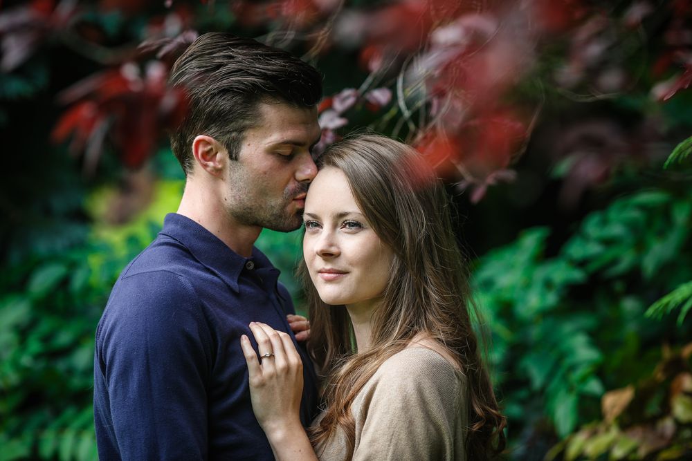 Young man kisses his fiancées forehead during a tender moment in the park