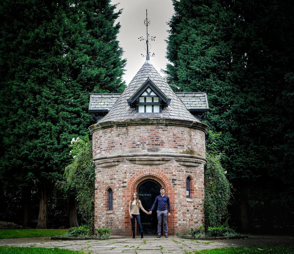 Engaged couple hold hands and stand before the Dovecoat building in Walkden gardens manchester