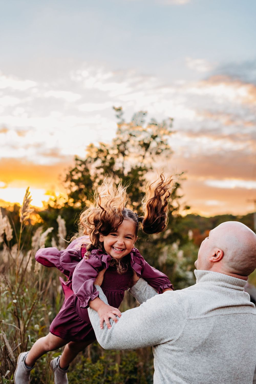 Candid sunset moment of playful interaction in field with hair blowing in wind and colorful sky.