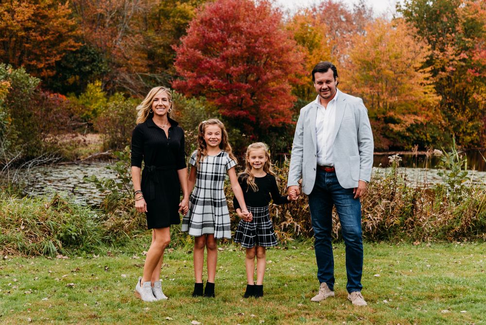 Family of four poses together against vibrant fall foliage background.