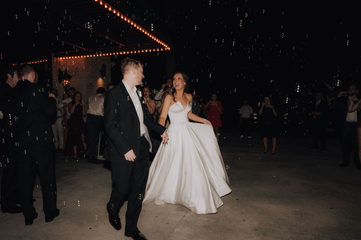 Couple makes their evening exit at wedding venue under twinkling lights.