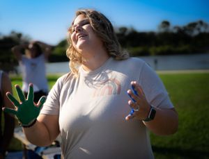 Paint-covered hands raised joyfully against a bright blue sky background.