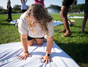 Group participants watching a colorful outdoor activity on a sunny day in a grassy park setting.