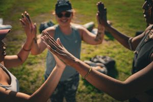 People raising their hands together in unity at an outdoor event with green scenery.