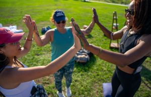 Various hands reaching out and connecting during an outdoor gathering in bright sunlight.