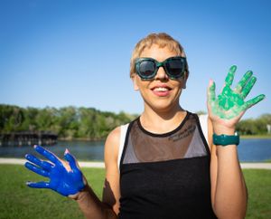 Hands painted in bright green and blue colors held up against clear blue sky.