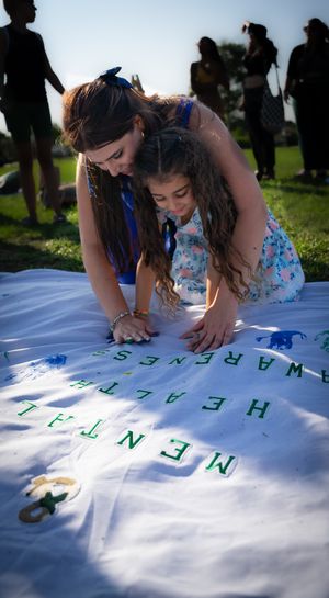 People creating handprints on a white banner spread out on grass during an outdoor event.