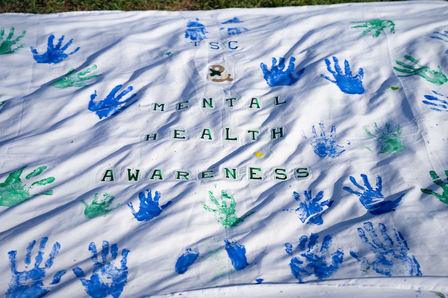 Blue and green handprints decorating a white banner with text outdoors.