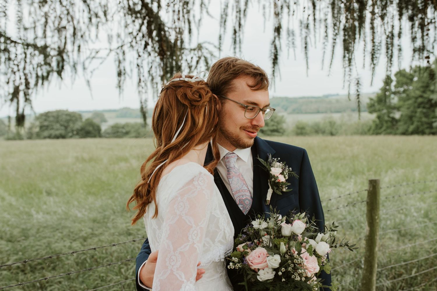 Romantic outdoor wedding moment with bride and groom embracing in a lush green field.