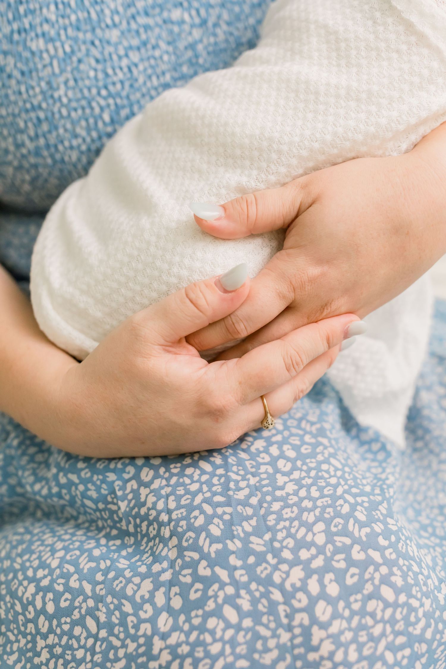 Gentle hands cradle a swaddled baby against a blue floral dress background.