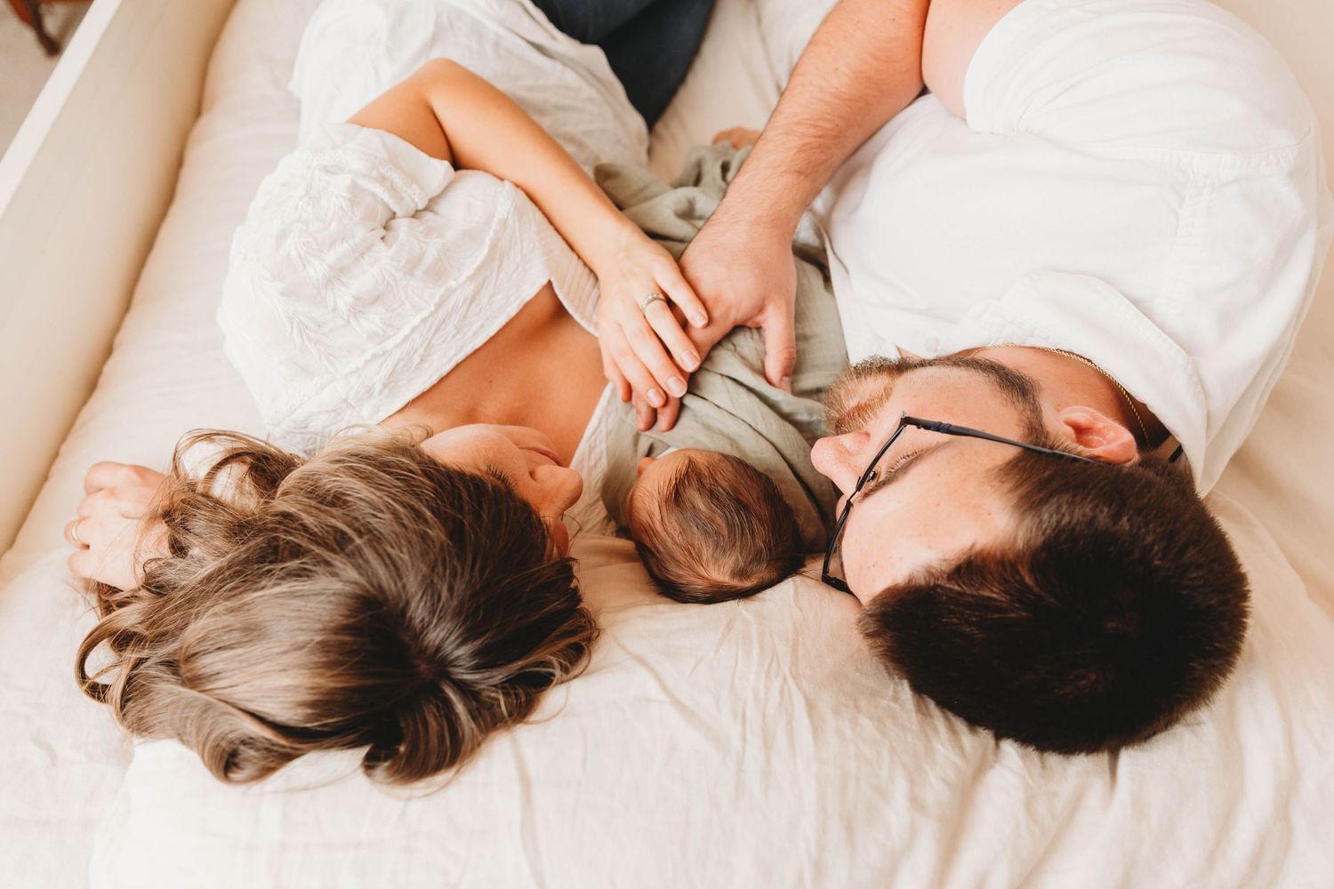 Family lying together on white bedding sharing an intimate moment at home.