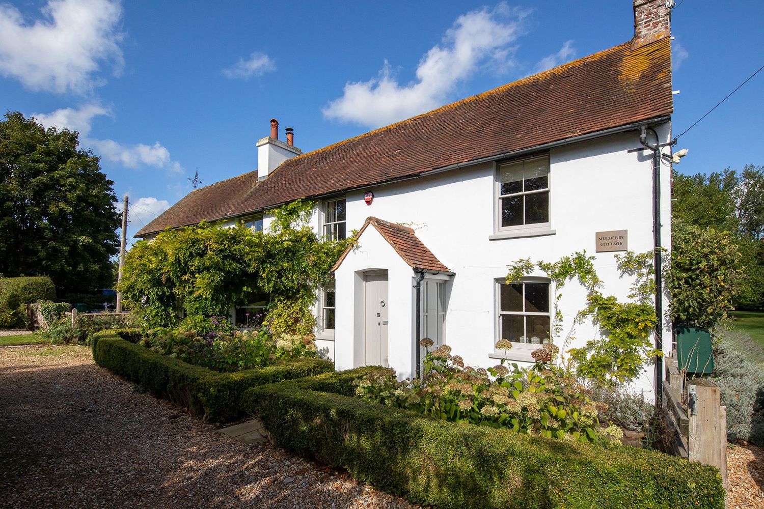 Charming white cottage with red tile roof and manicured garden entrance.
