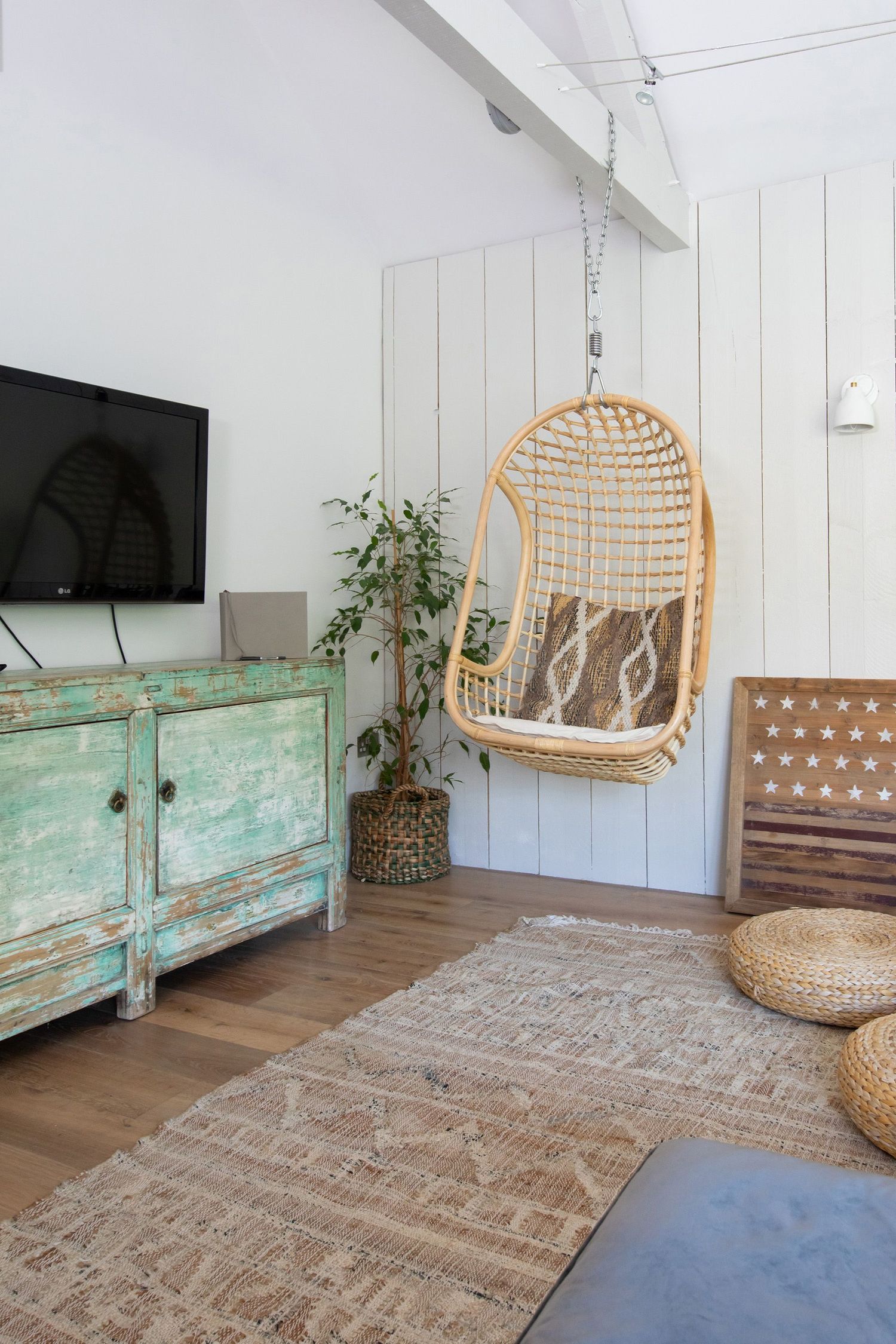 Modern boho living room with hanging rattan chair and distressed turquoise media cabinet.