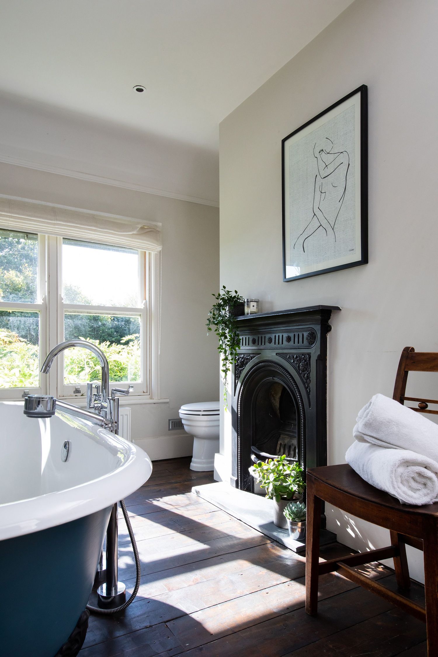Elegant bathroom featuring a freestanding clawfoot tub, black fireplace, and large windows.