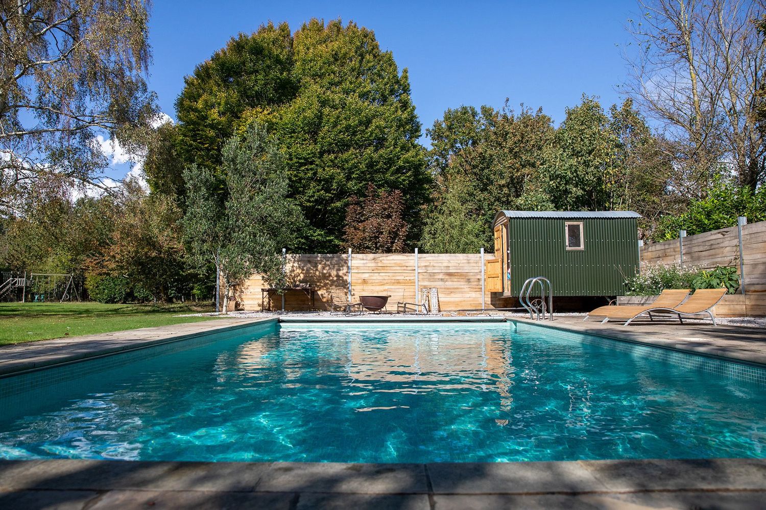 Large swimming pool with turquoise water surrounded by trees and stone patio.
