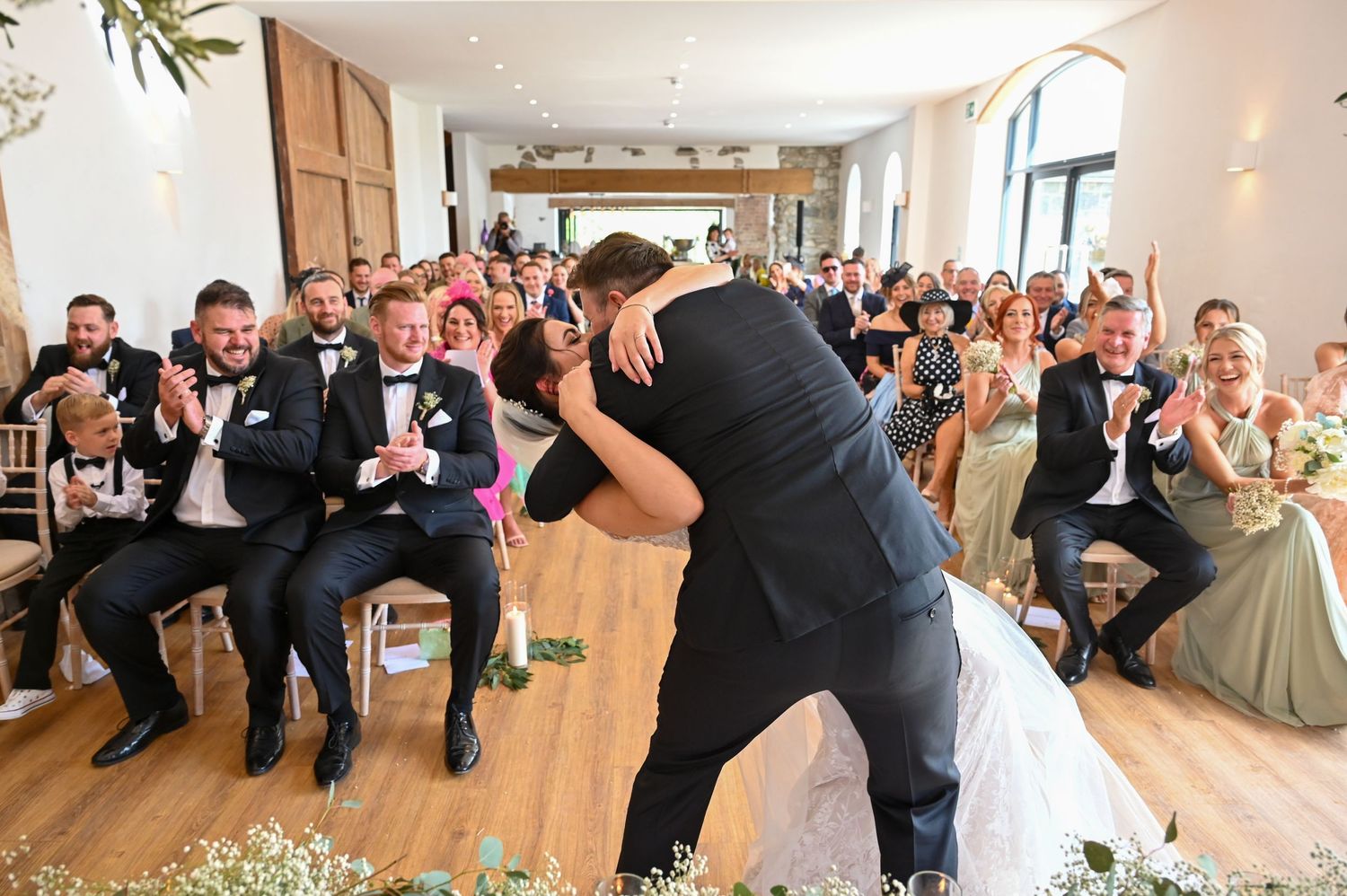 Wedding reception celebration with couple performing dramatic dance move on wooden floor.