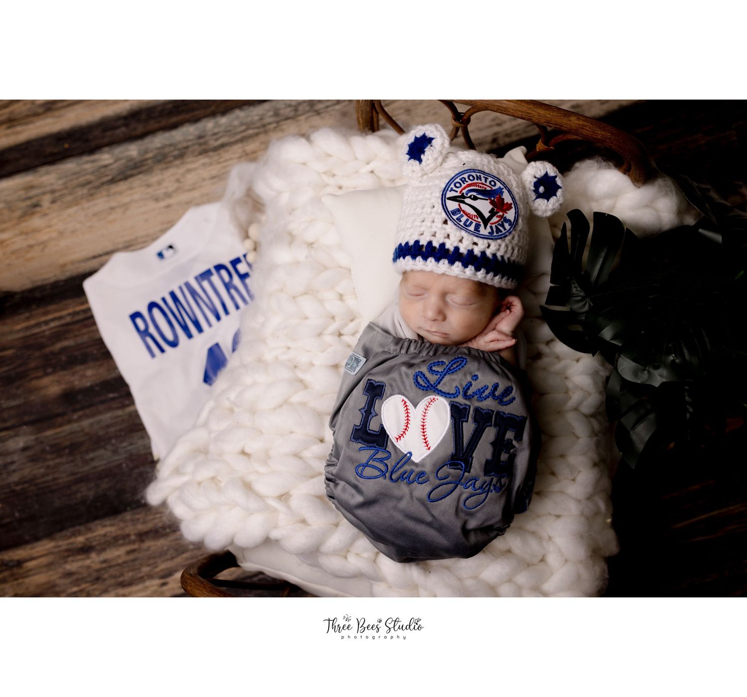 Newborn in baseball-themed setting with team merchandise and white fuzzy blanket.