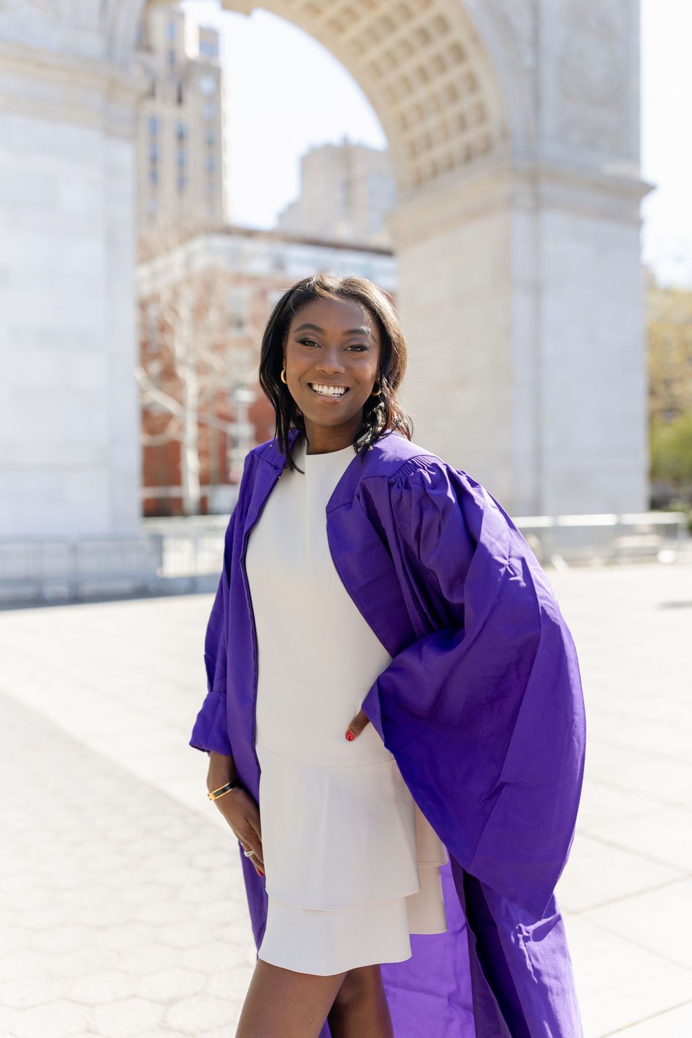 Beautiful graduation portrait under historic arch with purple regalia and white dress.