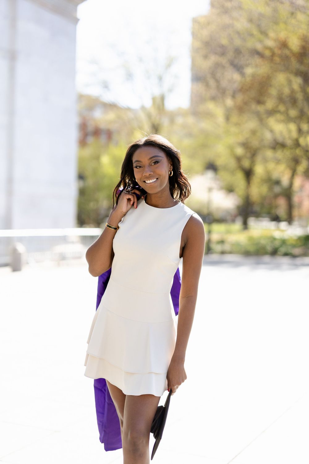 Joyful graduation portrait in white dress and purple gown near architectural arch.