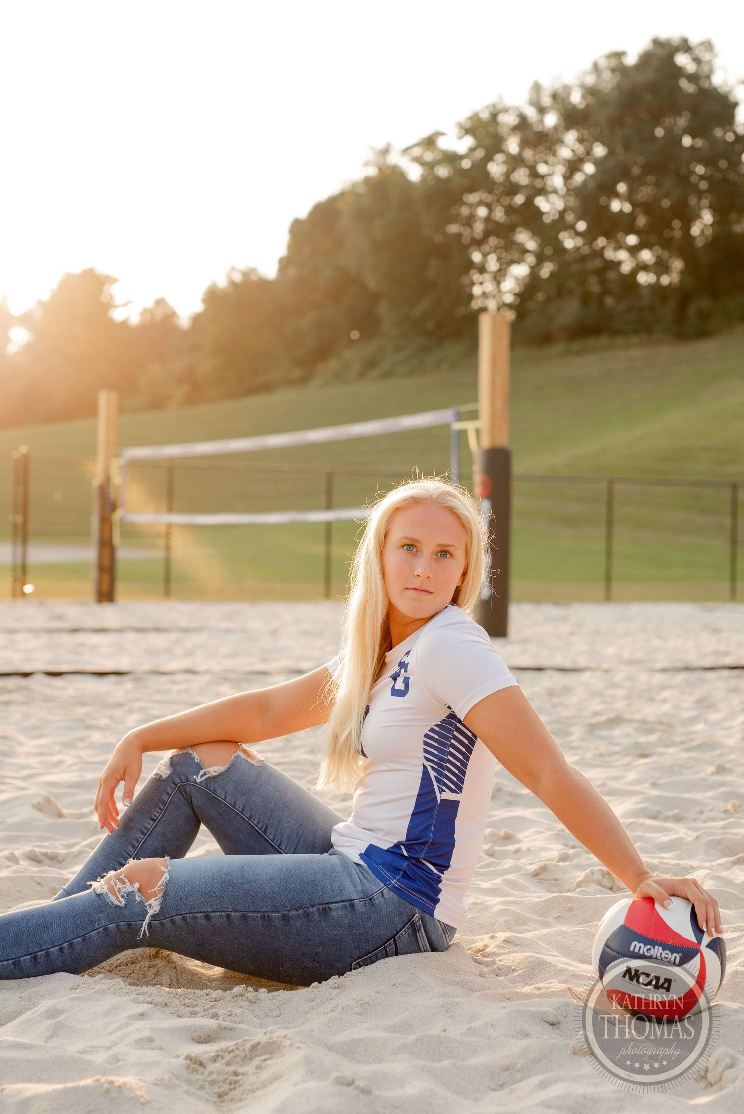 Player in white jersey relaxing on beach volleyball court with NCAA ball.
