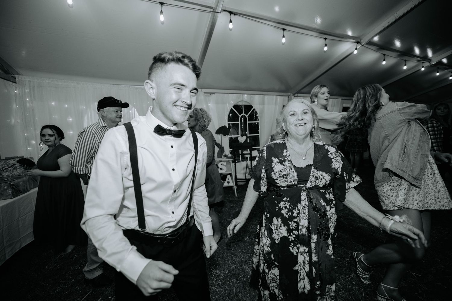 Wedding guests dancing and celebrating under string lights in a reception tent.
