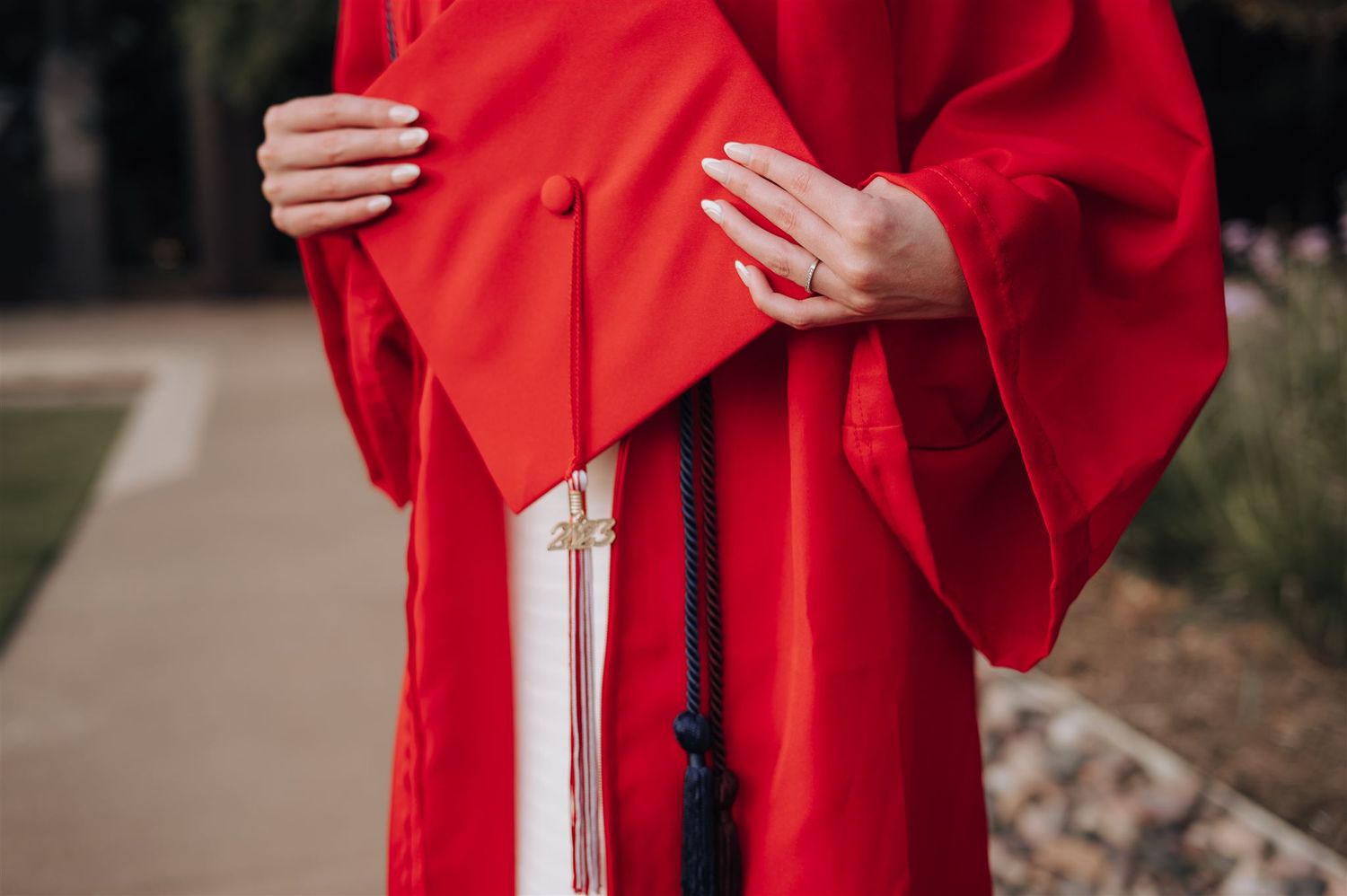 Close-up detail of hands holding a bright red graduation gown with white dress underneath.