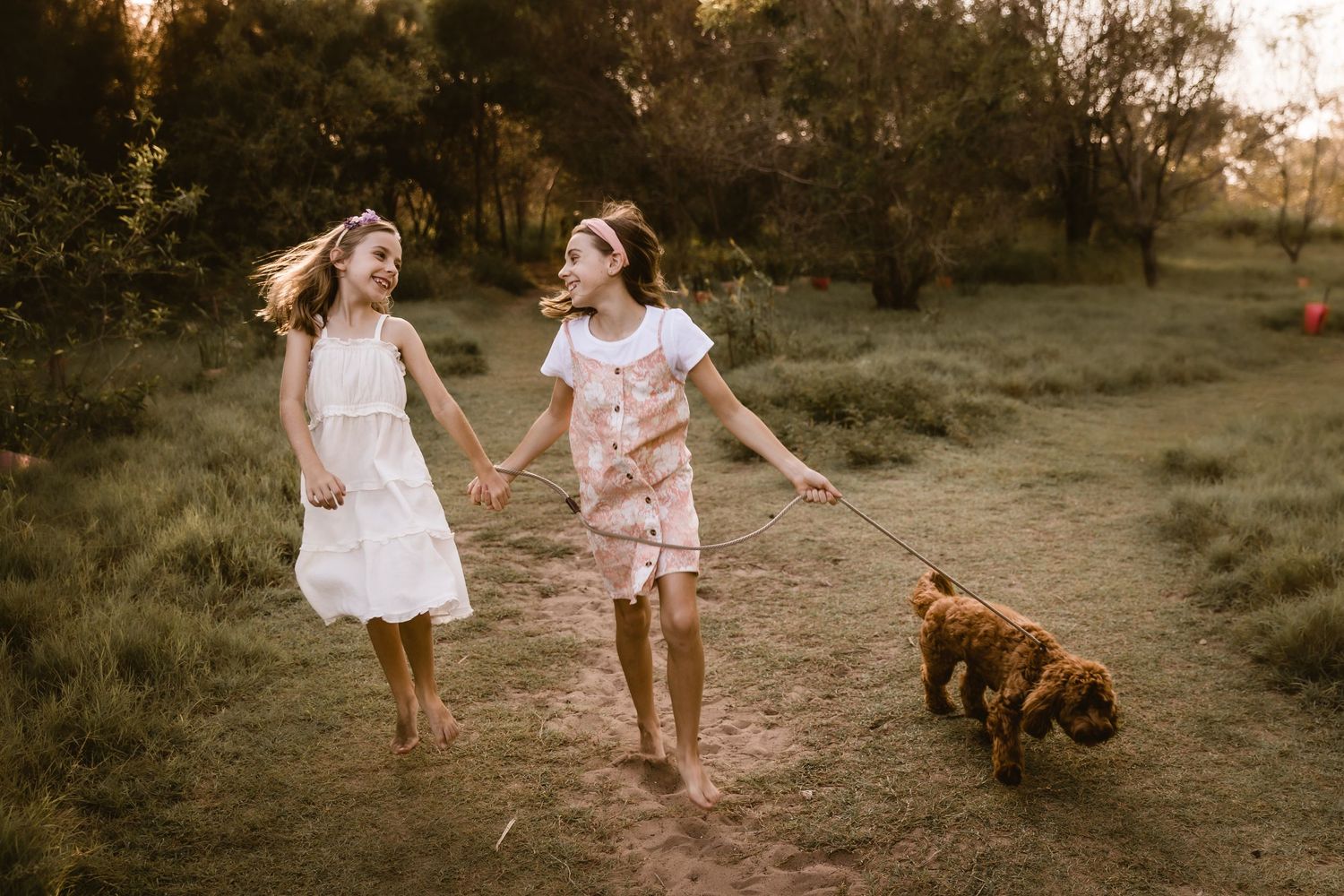 Two sisters holding hands and skipping with their family dog during a Brisbane family portrait shoot at the beach