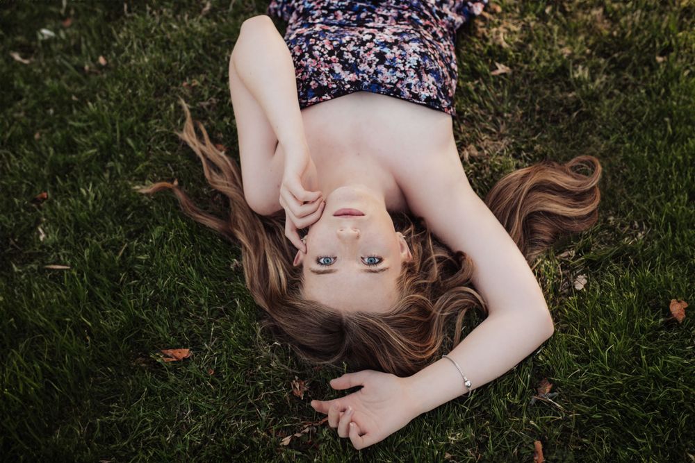 Artistic overhead portrait of someone lying in grass wearing a floral top.