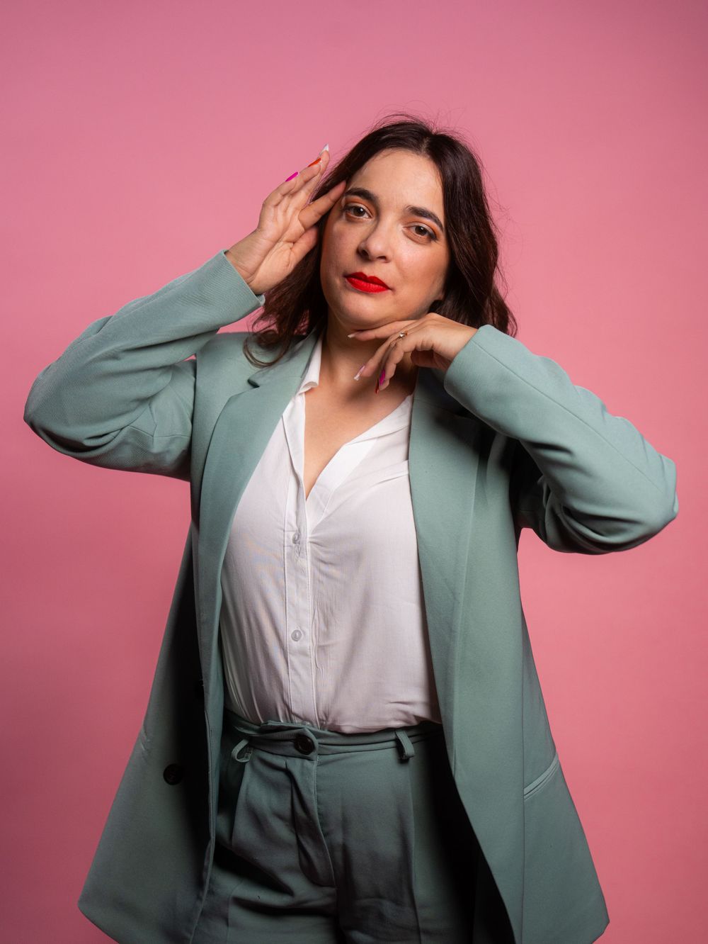 Professional portrait against pink backdrop wearing mint blazer and white blouse with dramatic poses.