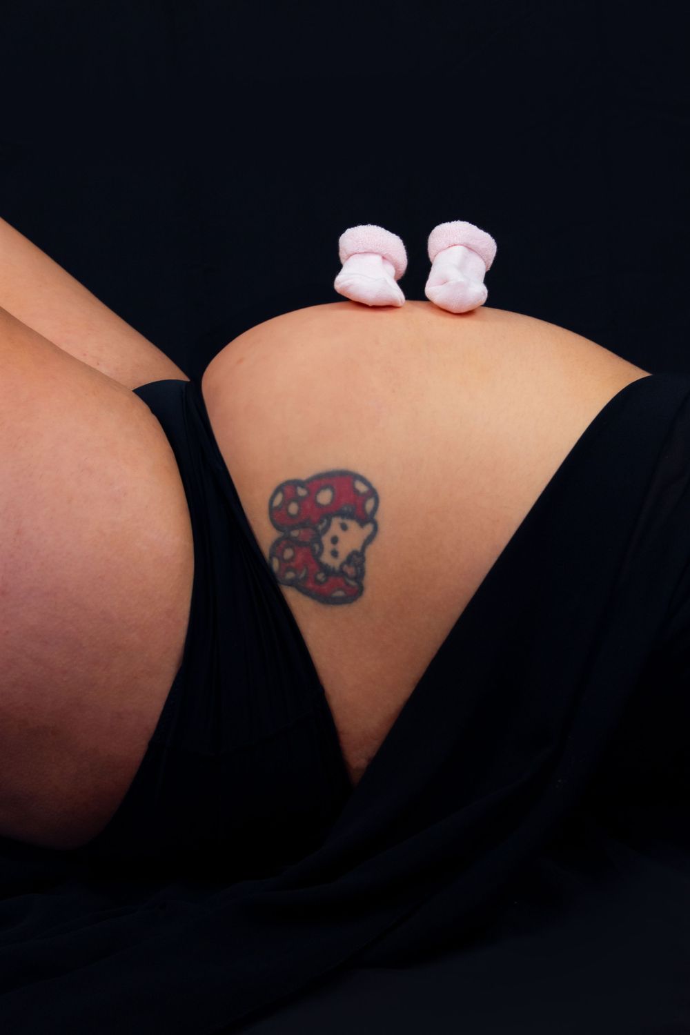Close-up details of baby socks and tattoo art in maternity photo series.