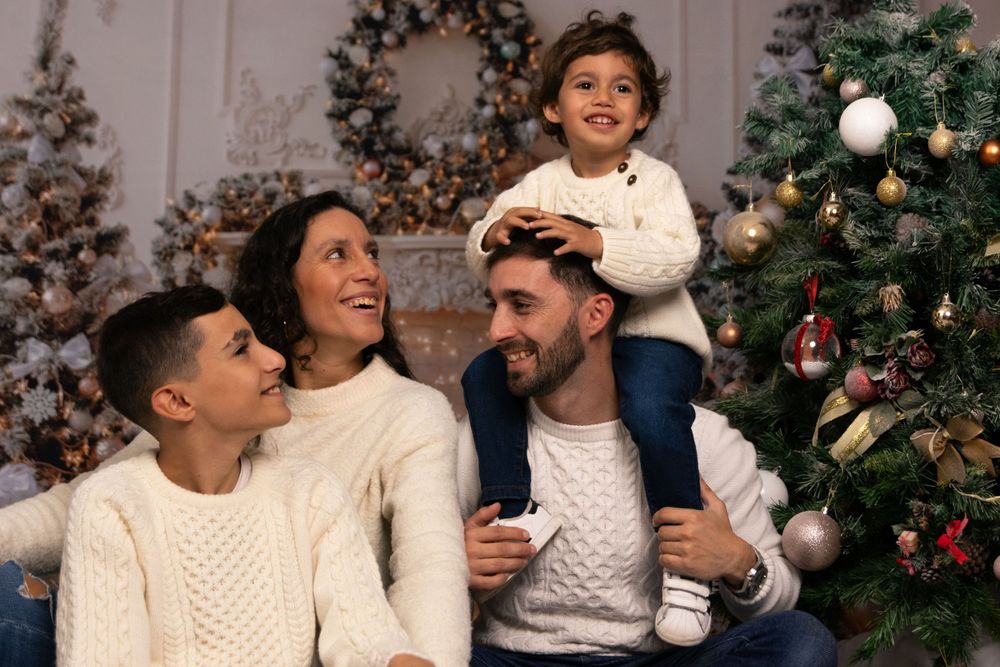 Candid holiday moment of family laughing together in matching white sweaters by Christmas decorations.