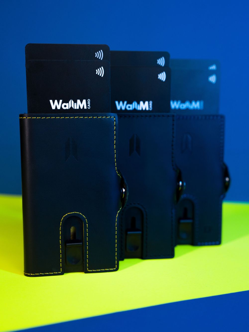 Three black contactless payment cards and wallets arranged on blue and green background.