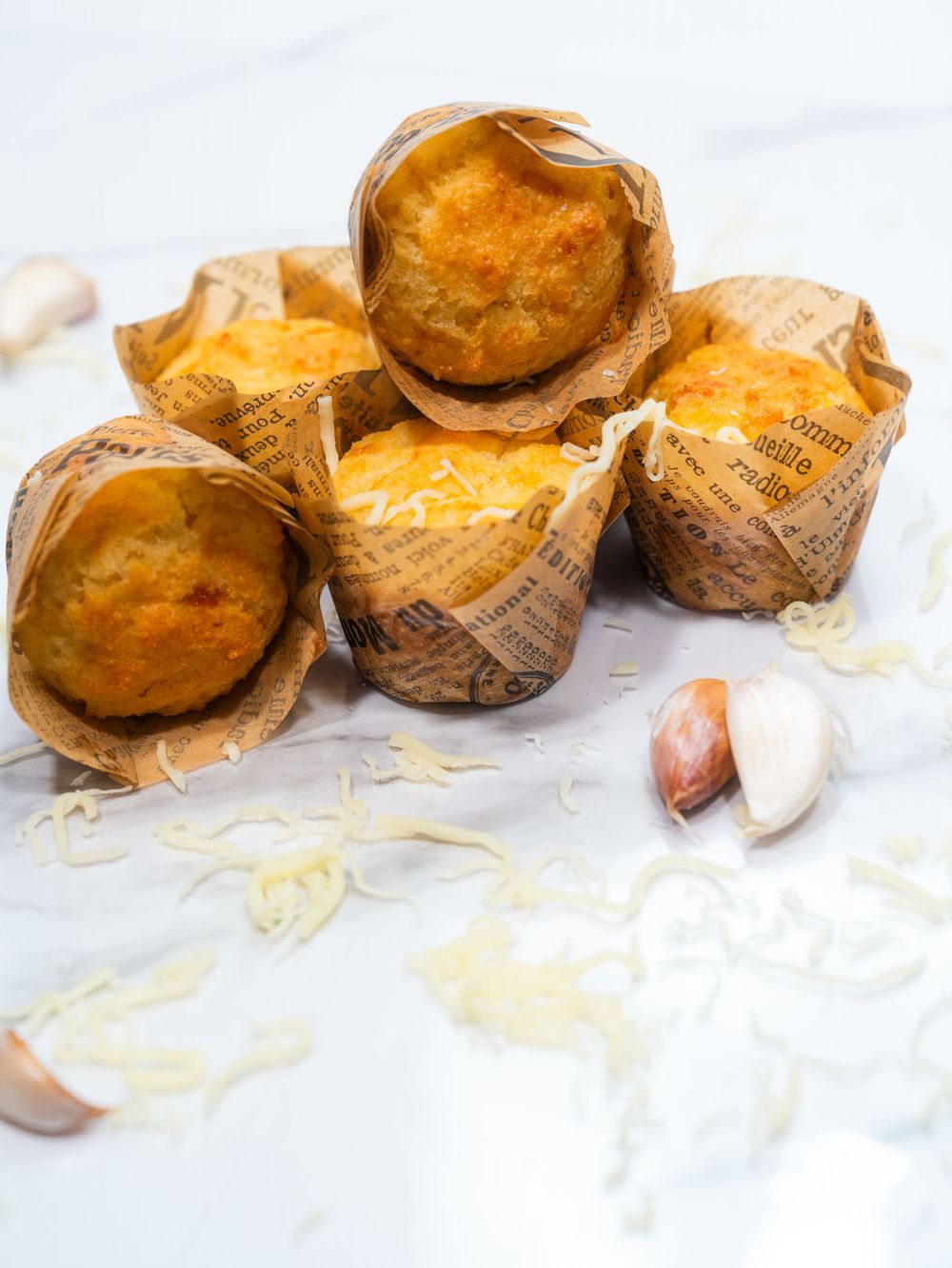 Freshly baked muffins wrapped in newspaper-style paper with garlic cloves.