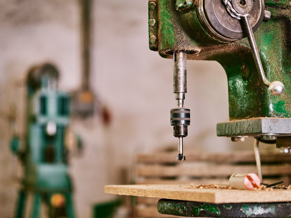 Close-up of an industrial green drill press machinery in operation.