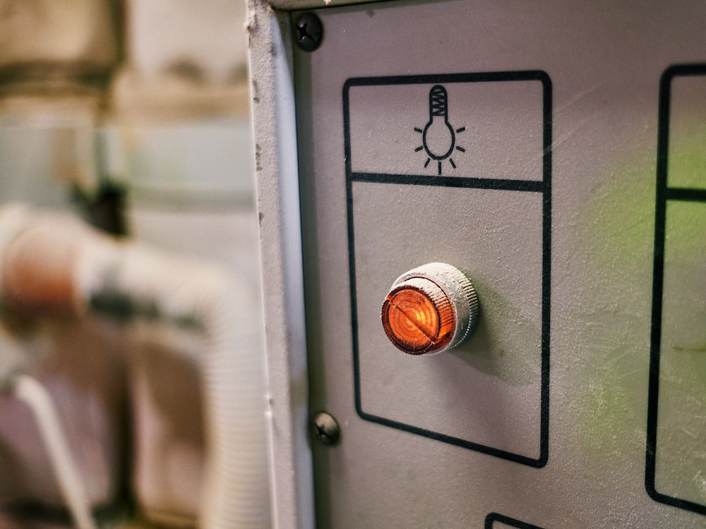 Orange power button with light bulb icon on industrial control panel.