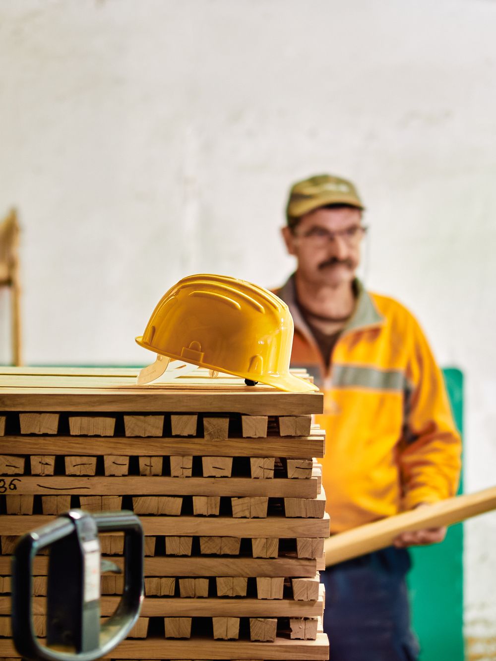 Yellow hard hat rests on stacked lumber with construction worker in background.
