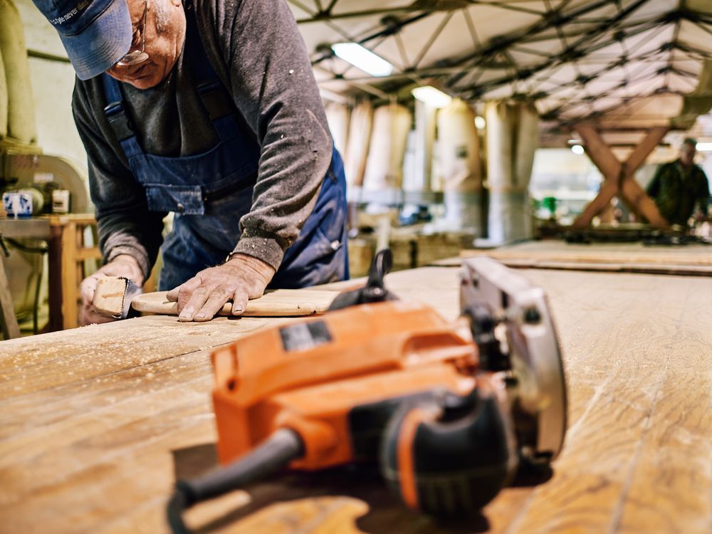Craftsman working with power tools on wooden surface in workshop environment.