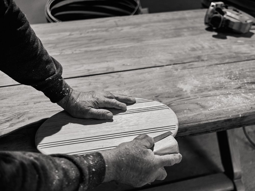 Close-up black and white shot of hands shaping wooden ski equipment on workbench.