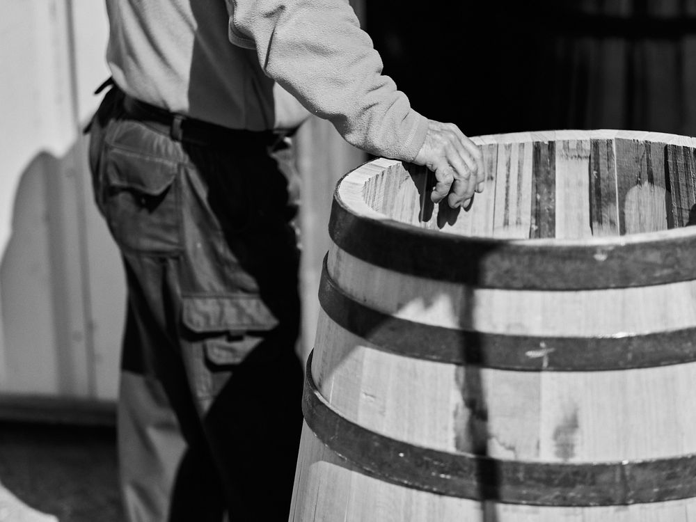 Hands inspecting a vintage wooden barrel with dark metal bands in black and white.