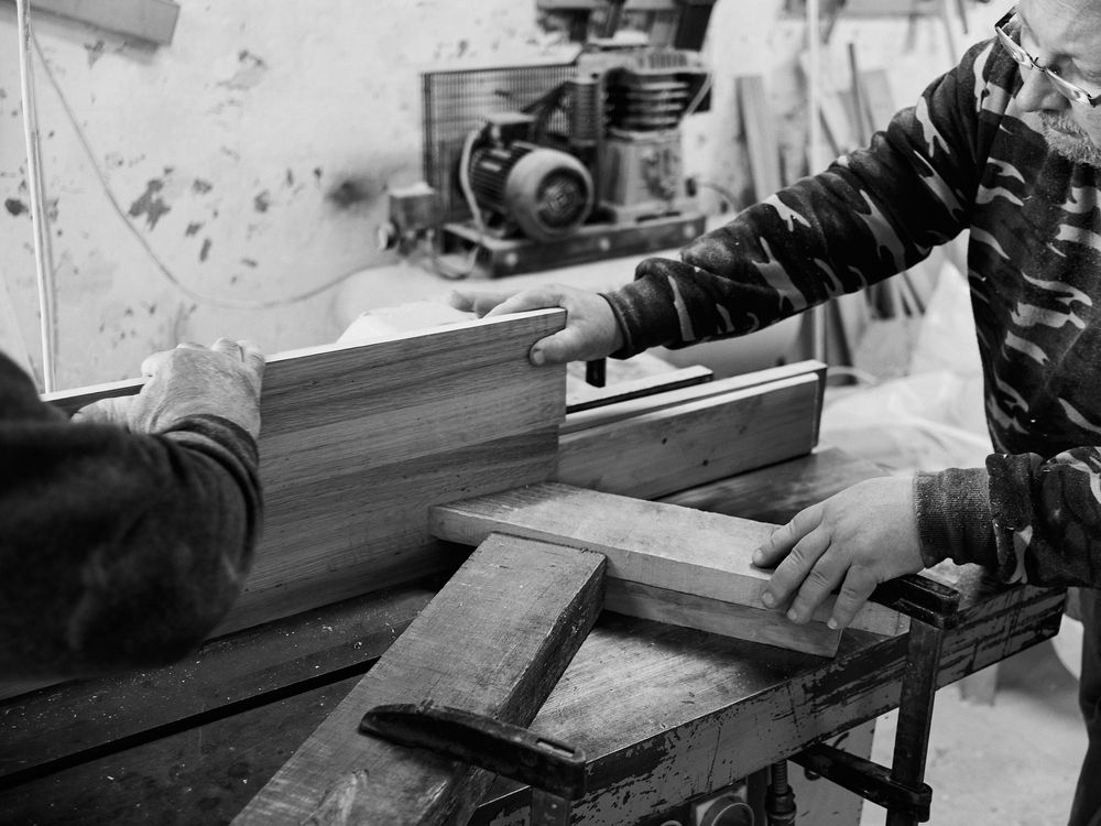 Craftsmen working with woodworking tools on a workbench in a black and white workshop scene.