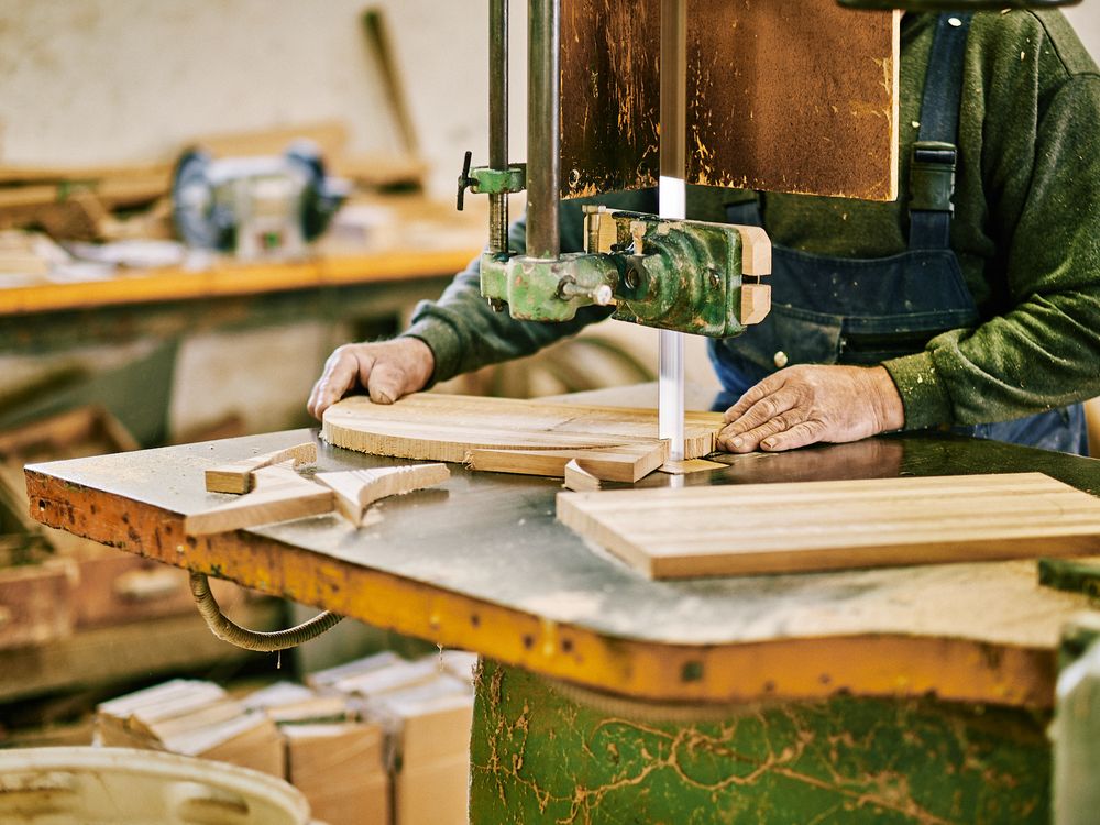Woodworker using bandsaw to cut wooden planks in workshop.