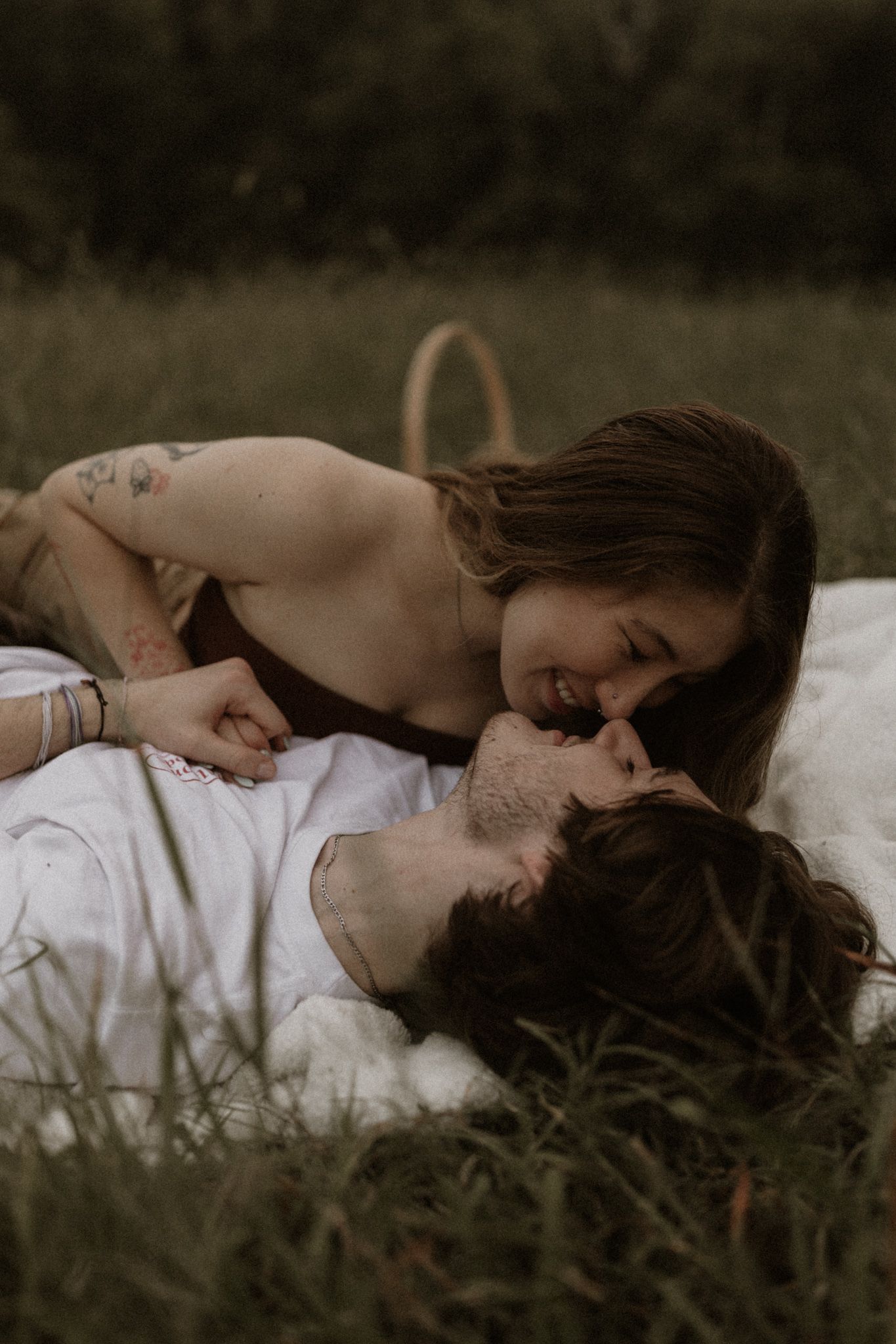 A romantic moment captured on a blanket in tall grass during golden hour.