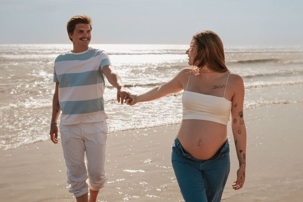 Couple holding hands while walking on sunlit beach.