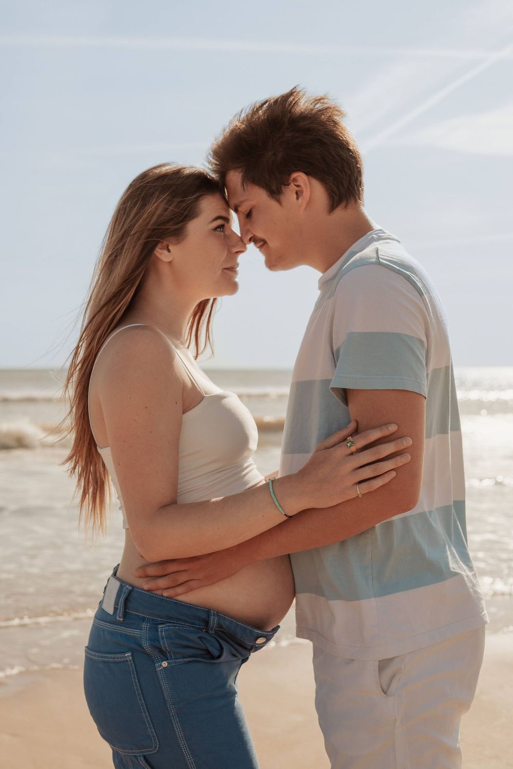Intimate couple embracing on beach during maternity photoshoot.
