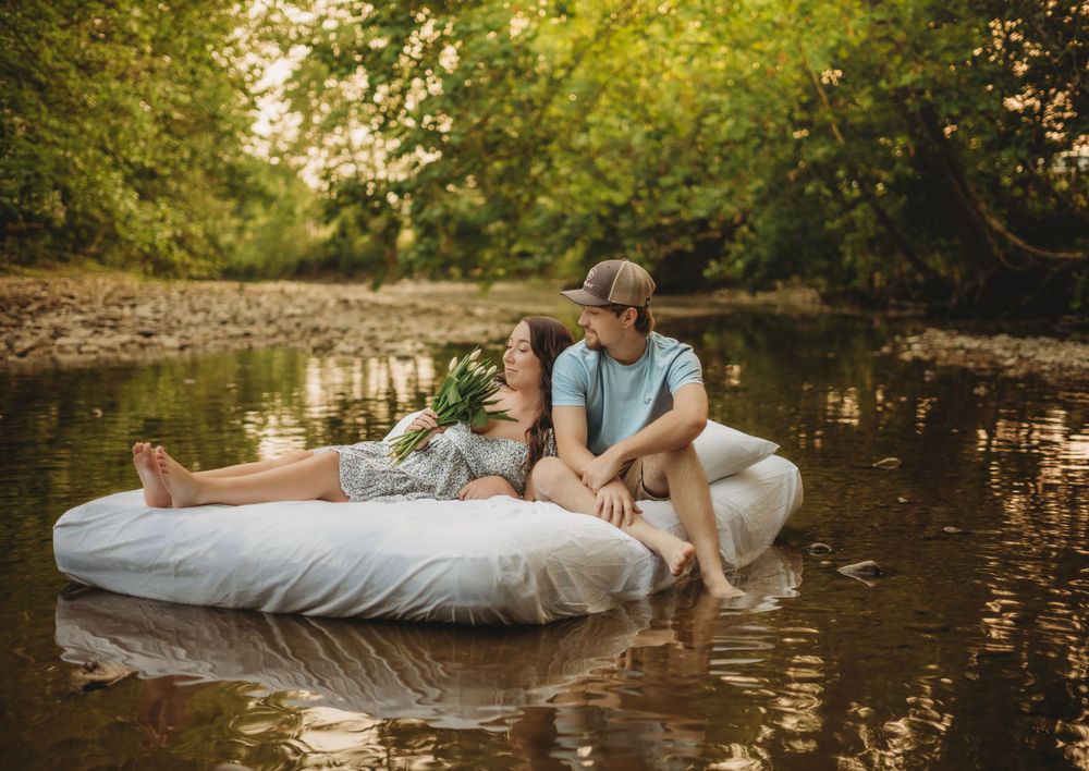 A couple relaxes on an air mattress floating in a serene pond at sunset.