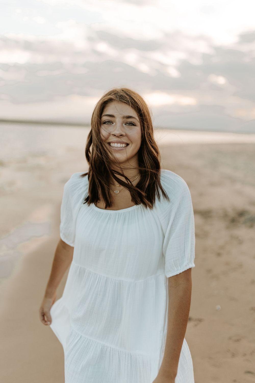 Woman in white dress smiling on beach at sunset with natural lighting and warm tones.